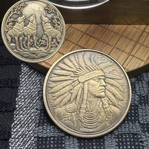 May include: Two antique-style coins. One coin features three wolves howling at the moon. The other coin depicts a Native American chief in profile, wearing a feathered headdress. Both coins have a bronze finish.