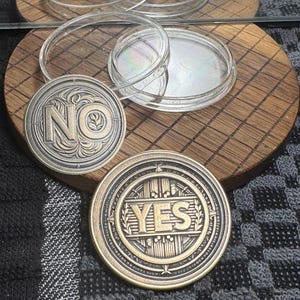 May include: Two metal decision coins, one with "NO" and the other with "YES" in raised lettering, sit on a wooden surface. Clear, circular petri dishes are also present. The "YES" coin has a gold finish, while the "NO" coin has a silver finish.