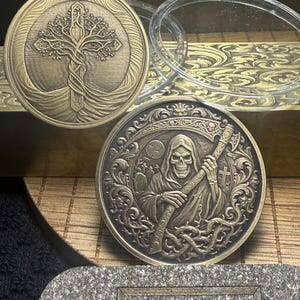 May include: Two circular brass-colored metal coins featuring intricate relief designs. One coin displays a tree intertwined with a cross, while the other depicts a hooded skeleton figure holding a scythe in a graveyard setting with a full moon.