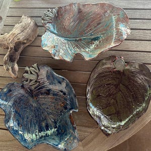 Puede incluir: Tres cuencos de cerámica con forma de hoja con un acabado esmaltado. Los cuencos están decorados con ranas y tienen un aspecto rústico y terroso.