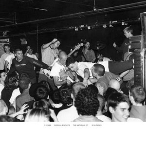 May include: Black and white photograph of a live music performance. A band plays on stage while the crowd interacts with the performers. The image captures a moment of energy and engagement between the band and the audience.