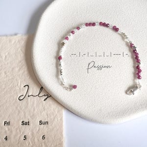 Könnte beinhalten: Ein silbernes Armband mit rosa und weißen Perlen. Das Armband hat einen Verschluss und das Wort "Passion" ist auf einer weißen Oberfläche hinter dem Armband geschrieben.