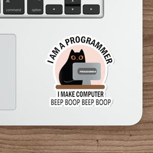May include: A white sticker with the text "I AM A PROGRAMMER" and "I MAKE COMPUTER BEEP BOOP BEEP BOOP". The sticker features a black cat sitting in front of a computer screen.