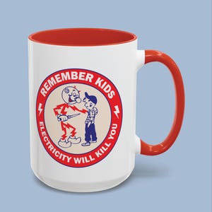 May include: A white ceramic mug with a bright red interior and handle. The exterior features a circular graphic with a red border containing a cartoon character made of lightning bolts holding a knife near a child, with the text REMEMBER KIDS ELECTRICITY WILL KILL YOU.