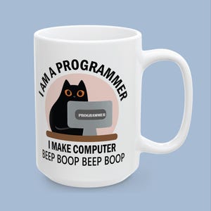 May include: A white ceramic mug featuring a graphic of a black cat sitting at a computer. The text reads I AM A PROGRAMMER above the cat and I MAKE COMPUTER BEEP BOOP BEEP BOOP below. The computer screen displays the word PROGRAMMER.