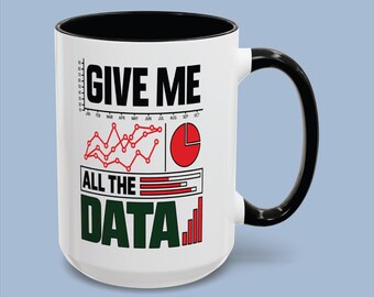 May include: A white ceramic mug with a black interior and handle. The front features the text GIVE ME ALL THE DATA in black and green, accompanied by red line graphs, a red pie chart, and a red bar chart representing various data visualisations.