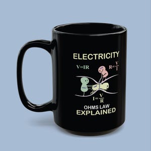 Puede incluir: Una taza de cerámica negra con una ilustración gráfica de la Ley de Ohm. El diseño incluye el texto ELECTRICITY y OHMS LAW EXPLAINED, junto con las fórmulas V=IR, R=V/I e I=V/R, representadas con tres pequeños personajes de dibujos animados etiquetados como Volt, Amp y Ohm.