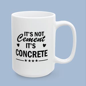 May include: A white ceramic mug featuring black text that reads IT'S NOT Cement IT'S CONCRETE, flanked by two small black hearts on the sides and a horizontal line with four black stars centered underneath the text on the front of the mug.