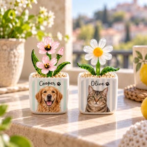 May include: Two square ceramic planters with light blue stripes, each featuring a pet portrait and name. One shows a golden retriever named Cooper with pink glass flowers, the other a tabby cat named Olive with a white glass daisy.