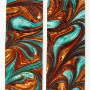 May include: Two rectangular pieces of marbled resin with a swirling pattern of teal, brown, and gold. The resin is translucent and has a glossy finish.