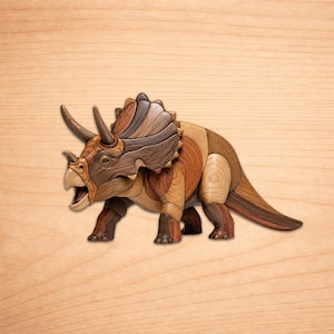 Op de afbeelding: Een houten Triceratops sculptuur met een gedetailleerd, meerkleurig ontwerp. De dinosaurus heeft een bruin, beige en grijs kleurenpalet, met zichtbare hoorns en een kraag. Het kunstwerk is geplaatst tegen een lichte houtnerf achtergrond.