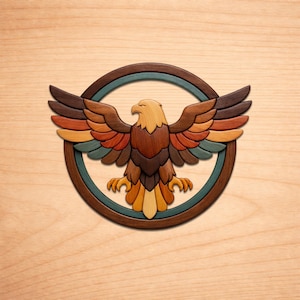 Puede incluir: Un emblema de águila de madera con las alas extendidas, elaborado con varios tonos de madera. El águila está centrada dentro de un círculo marrón oscuro con un anillo interior turquesa. Las plumas del águila muestran tonos de marrón, naranja, amarillo y turquesa.
