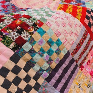 以下が含まれることがあります： さまざまな生地の模様と色を使用したパッチワークキルト。赤、青、緑、ピンク、黒の色合いの正方形、ひし形、ストライプが特徴です。正方形の中には花柄のものもあれば、幾何学模様のものもあります。
