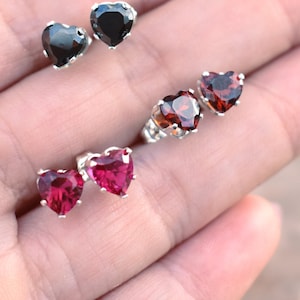 May include: Three pairs of heart-shaped earrings with silver posts. The earrings are black, red, and burgundy.