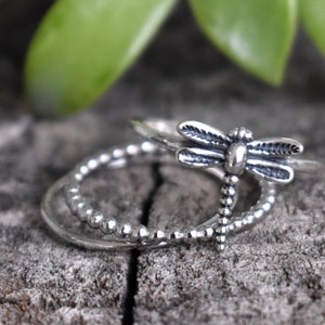 May include: Three silver rings, one with a dragonfly design and two with beaded bands.