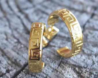May include: A pair of gold hoop earrings with a geometric pattern. The earrings are made of metal and have a shiny finish.