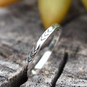 May include: A silver ring with a simple arrow design. The ring is on a wooden surface.