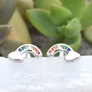 May include: A pair of silver rainbow earrings with a cloud design. The rainbow is made of colorful gemstones.