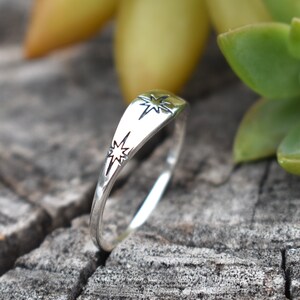 May include: A silver ring with two star designs. The ring is on a wooden surface.