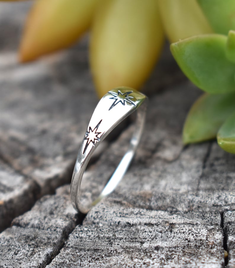 May include: A silver ring with two star designs. The ring is on a wooden surface.
