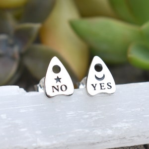 May include: A pair of silver earrings shaped like a witch's board with the words "YES" and "NO" on them.