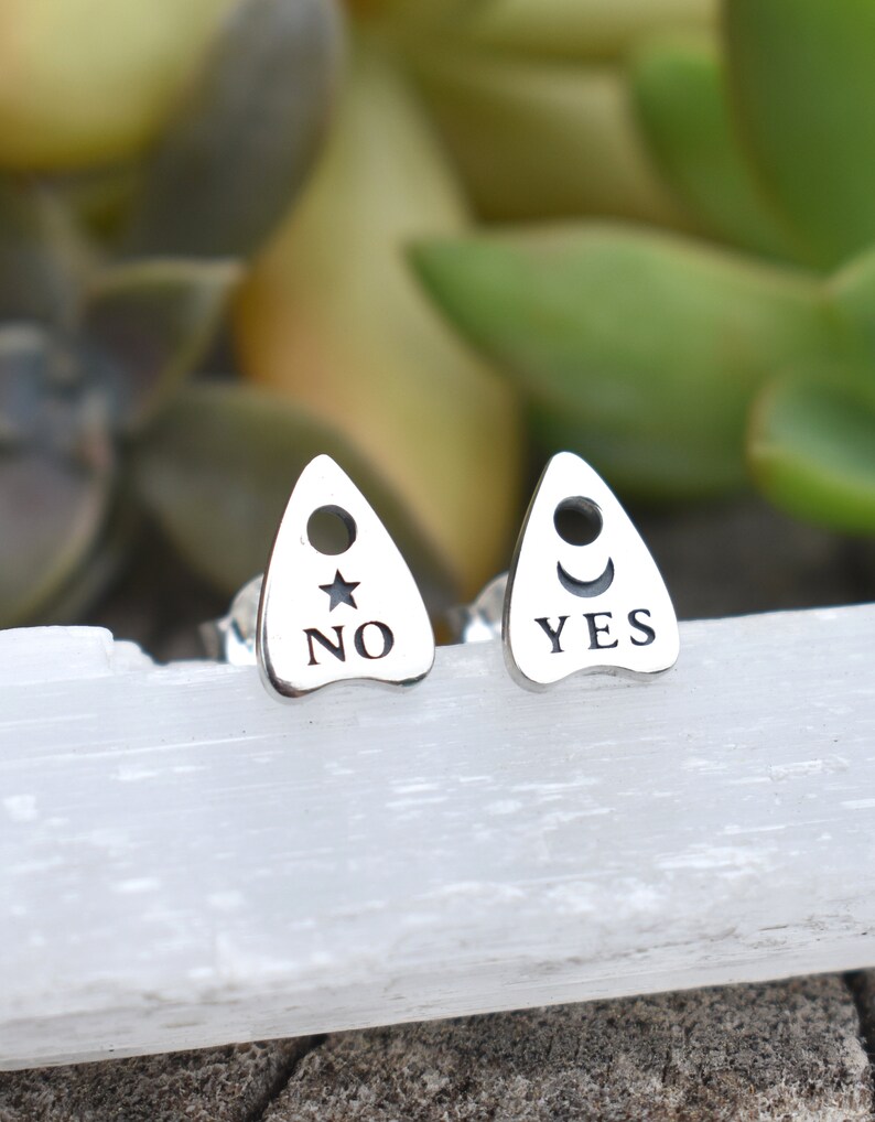 May include: A pair of silver earrings shaped like a witch's board with the words "YES" and "NO" on them.