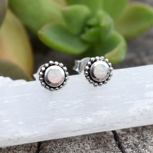 May include: A pair of silver stud earrings with a white opal gemstone in the centre of each earring. The earrings have a beaded border.