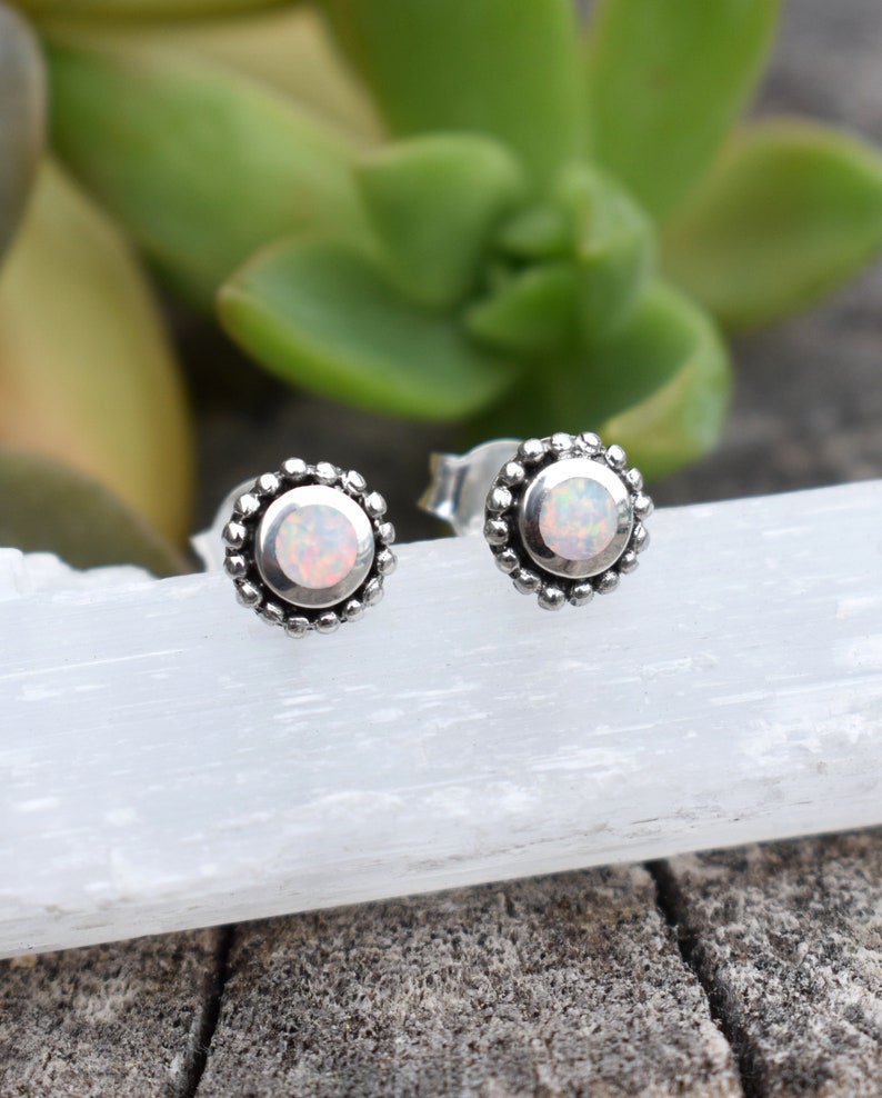 May include: A pair of silver stud earrings with a white opal gemstone in the centre of each earring. The earrings have a beaded border.