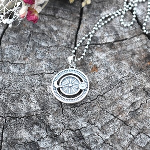 May include: A silver necklace with a circular pendant featuring a sun and moon design. The pendant has a textured surface and a detailed design.