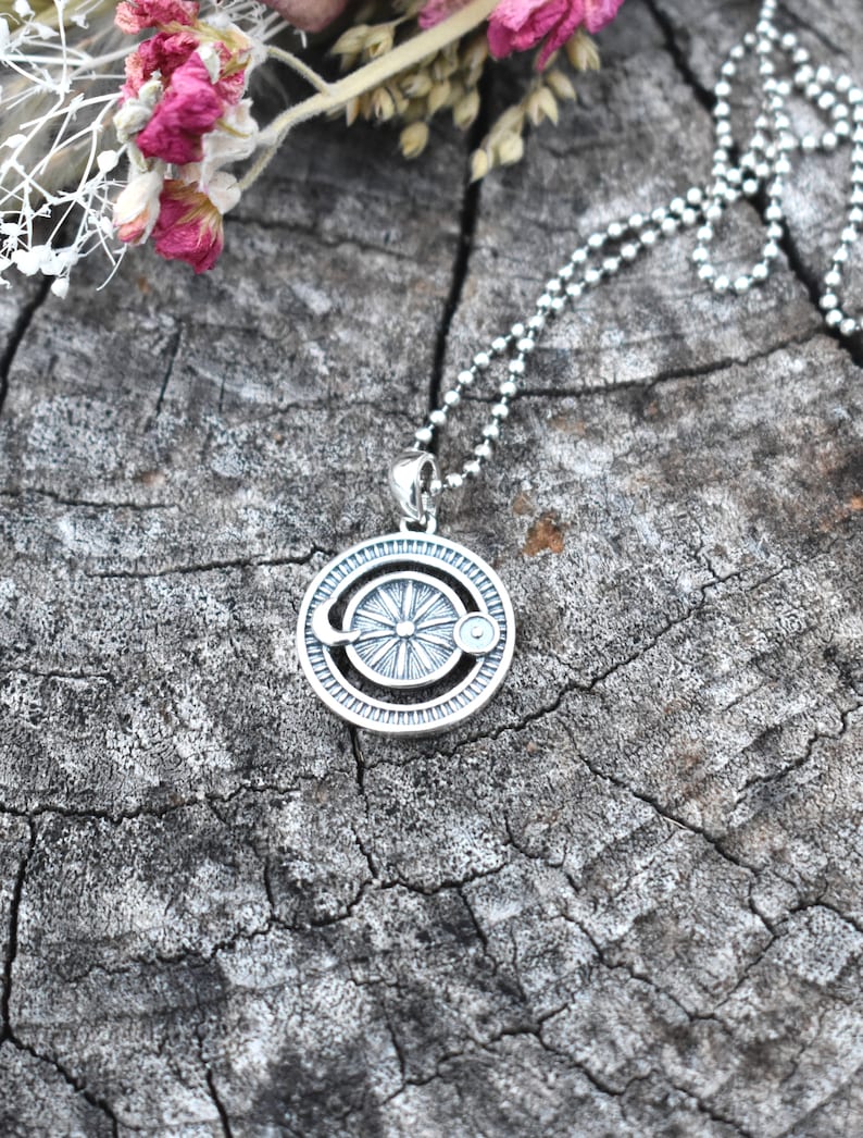 May include: A silver necklace with a circular pendant featuring a sun and moon design. The pendant has a textured surface and a detailed design.