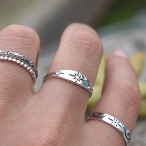 May include: Three silver rings with different designs. The top ring has a star design, the middle ring has a beaded design, and the bottom ring has a moon and star design.