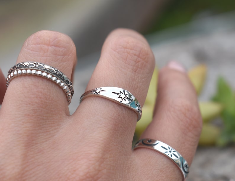 May include: Three silver rings with different designs. The top ring has a star design, the middle ring has a beaded design, and the bottom ring has a moon and star design.