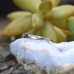 May include: A silver ring with a sunburst design. The ring is on a white rock.