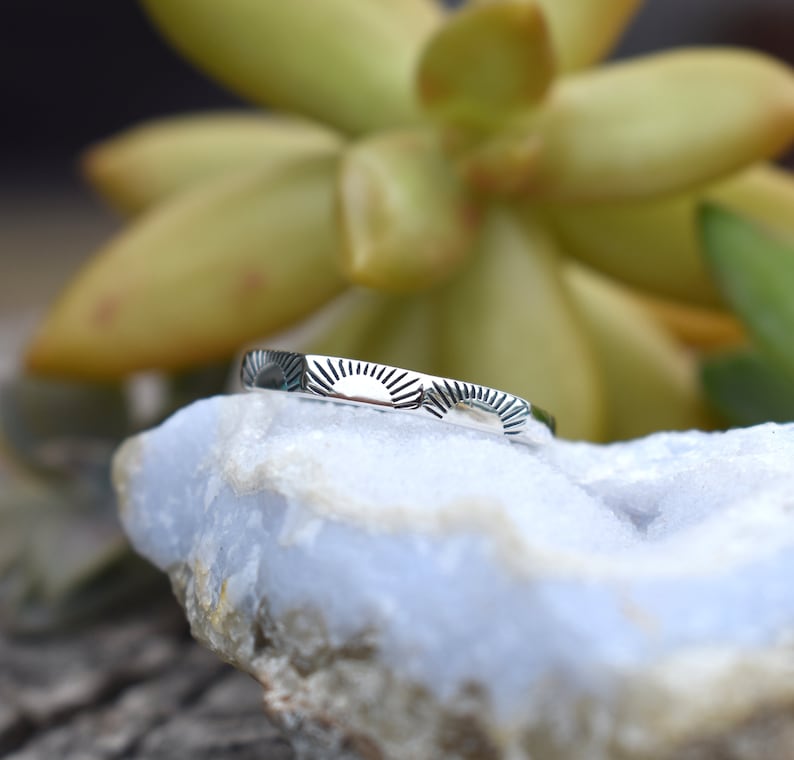 May include: A silver ring with a sunburst design. The ring is on a white rock.