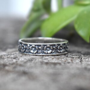 May include: A silver band ring with a floral design. The ring is made of sterling silver and features a delicate floral pattern.
