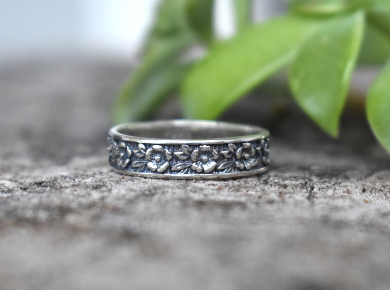 May include: A silver band ring with a floral design. The ring is made of sterling silver and features a delicate floral pattern.