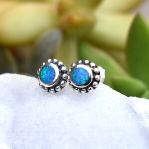 May include: A pair of silver stud earrings with blue opal gemstones. The earrings have a beaded border around the opal.