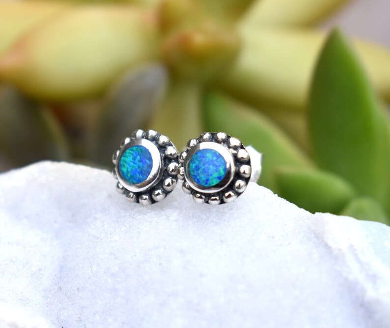 May include: A pair of silver stud earrings with blue opal gemstones. The earrings have a beaded border around the opal.