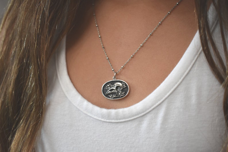 May include: A silver chain necklace with a pendant featuring a detailed skull with floral accents.