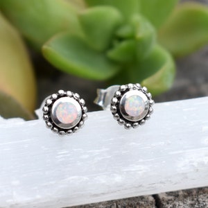 May include: A pair of silver stud earrings with a white opal gemstone in the centre of each earring. The earrings have a beaded border.