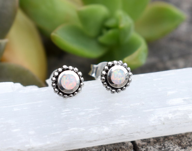 May include: A pair of silver stud earrings with a white opal gemstone in the centre of each earring. The earrings have a beaded border.