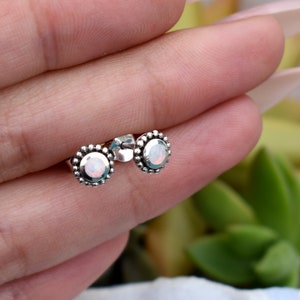 May include: A pair of silver stud earrings with a white opal gemstone in the centre of each earring. The earrings have a beaded border around the gemstone.