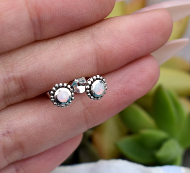 May include: A pair of silver stud earrings with a white opal gemstone in the centre of each earring. The earrings have a beaded border around the gemstone.