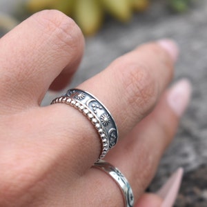 May include: A silver ring with a design of moons, stars, and suns. The ring is worn on a finger.