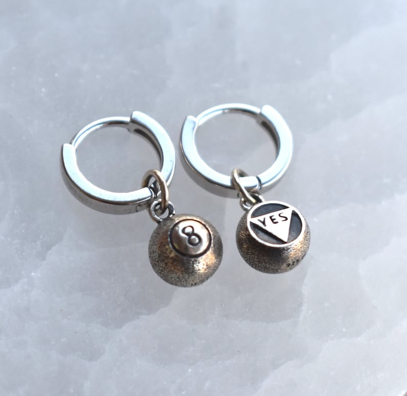 May include: A pair of silver hoop earrings with a silver charm hanging from each hoop. The charms are both silver billiard balls, one with the number 8 and the other with the word "YES" inscribed on it.