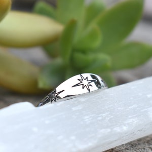 May include: A silver ring with a starburst design. The ring is on a white surface.