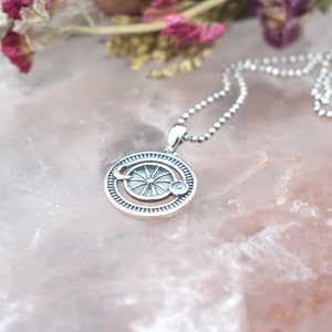 May include: A silver necklace with a circular pendant featuring a sun and moon design. The pendant has a detailed, intricate design with a sun in the center and a crescent moon on the side.