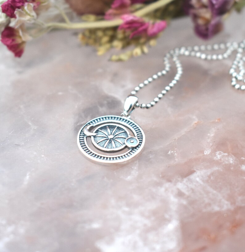May include: A silver necklace with a circular pendant featuring a sun and moon design. The pendant has a detailed, intricate design with a sun in the center and a crescent moon on the side.