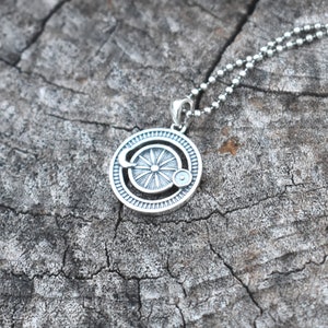 May include: A silver necklace with a circular pendant featuring a stylized sun with a crescent moon and a small circle around it. The pendant is on a silver chain.