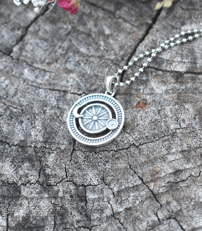 May include: A silver necklace with a circular pendant featuring a stylized sun with a crescent moon and a small circle around it. The pendant is on a silver chain.
